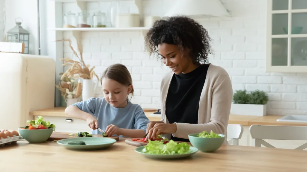 A young girl and her Au Pair chop vegetables in the kitchen
