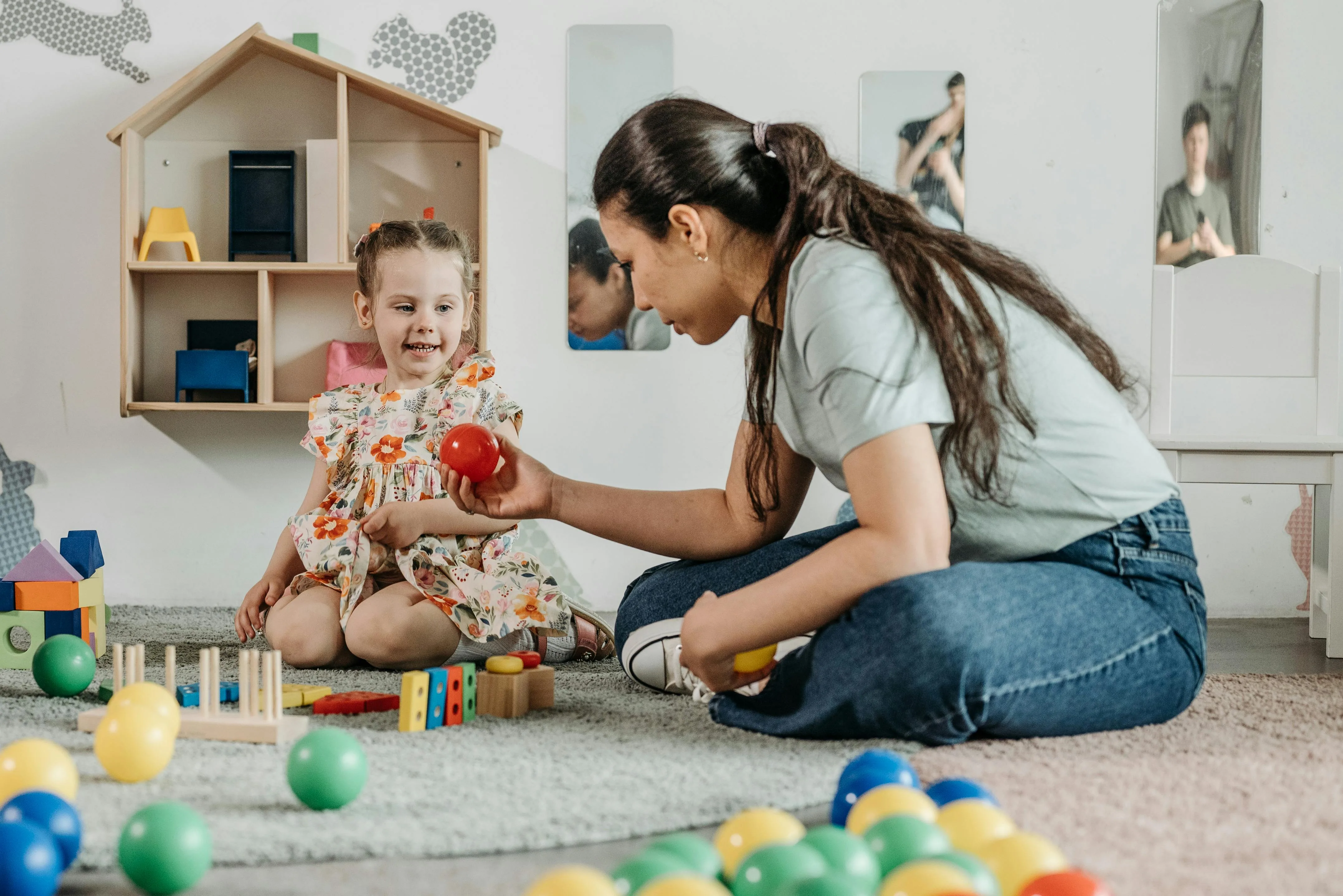 Au Pair and child sit on the floor playing with toys