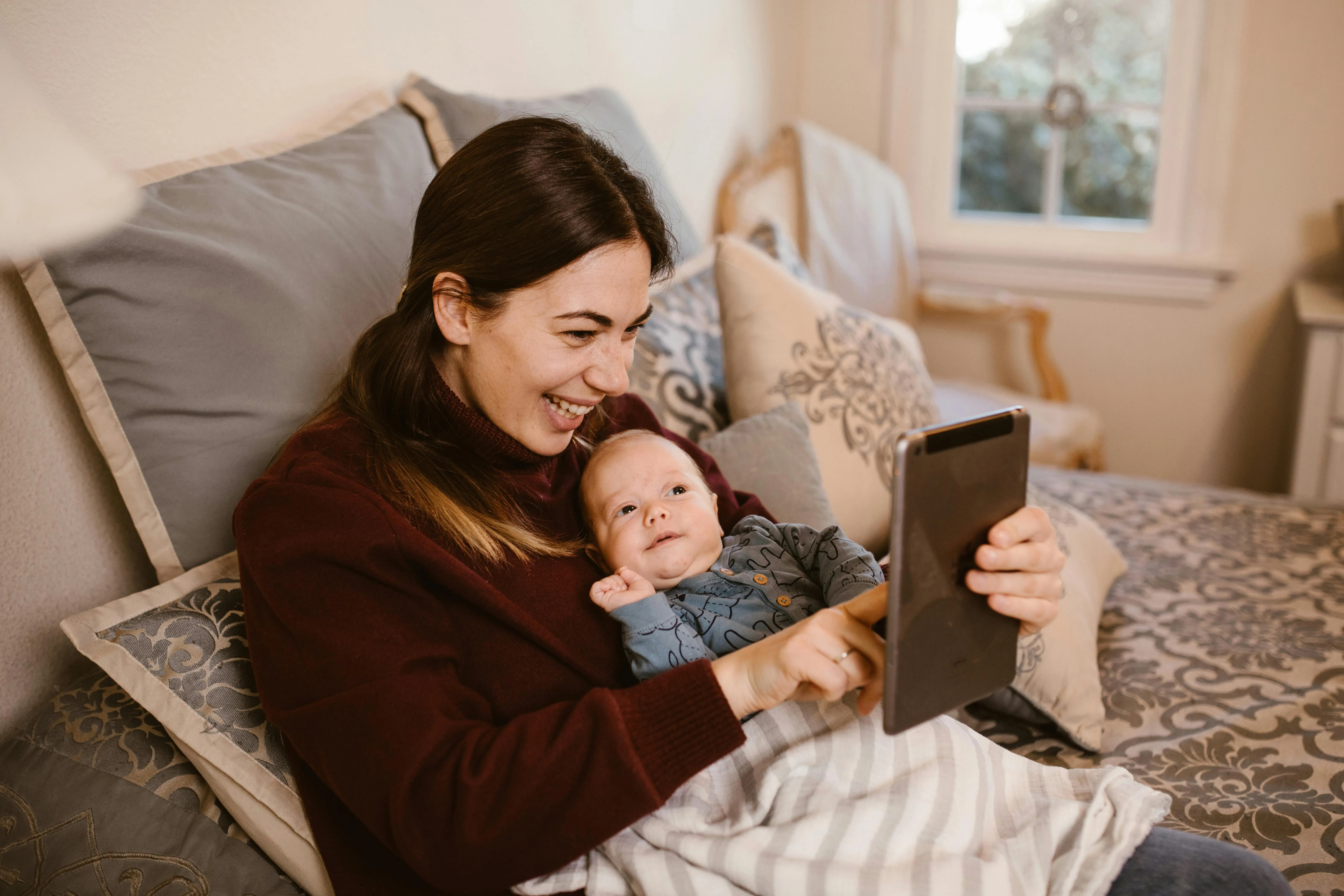 Au Pair checking daily schedule on tablet while holding baby