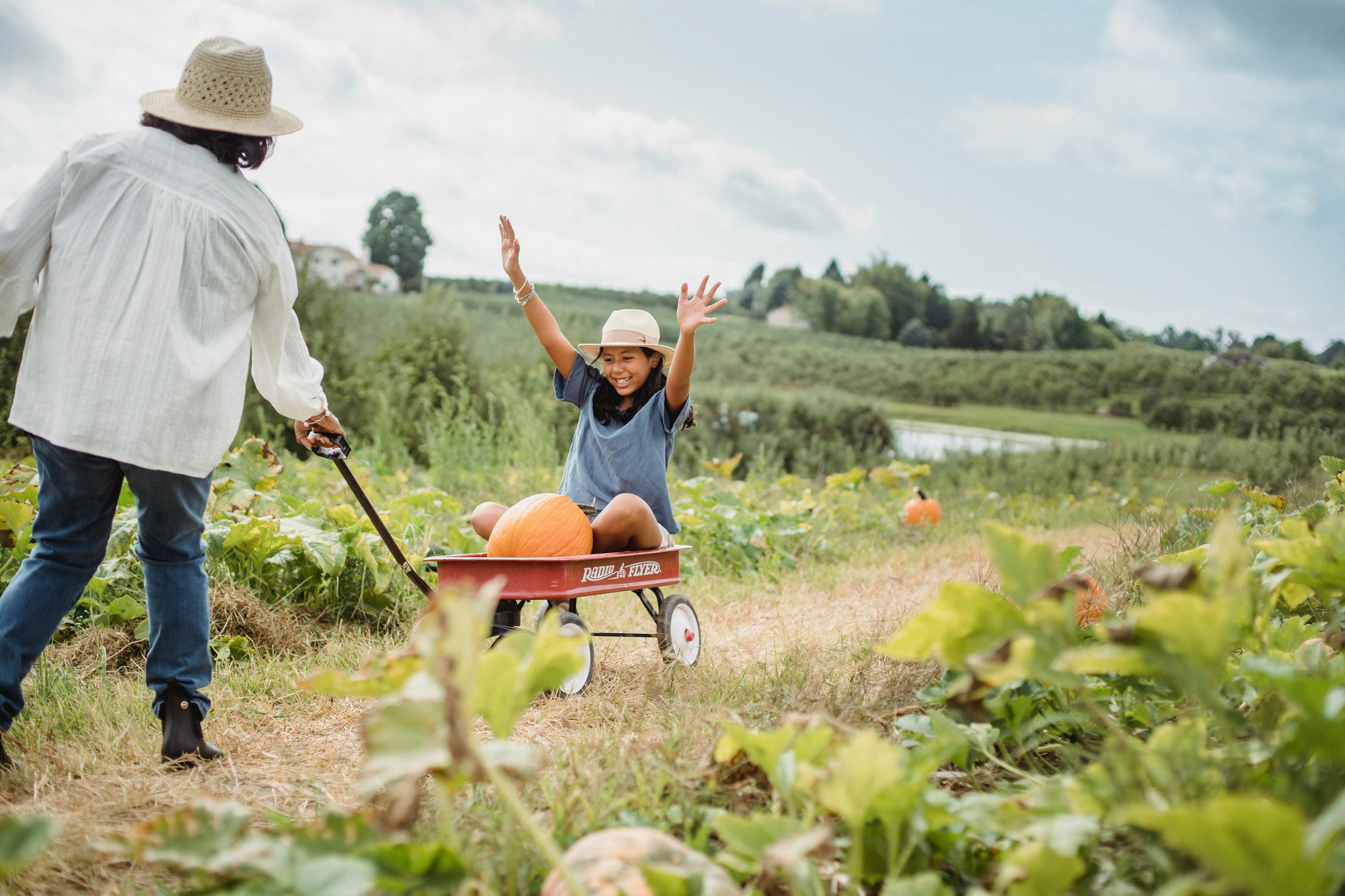 Au Pair pulls young girl on a wagon in a pumpkin patch